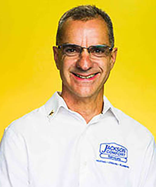 Man Wearing Glasses And A White Shirt With A &Quot;Jackson Comfort&Quot; Logo, Smiling, Representing Our Team In Front Of A Yellow Background.