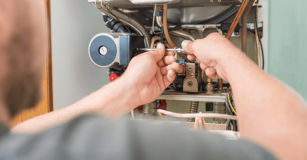 Hvac Technician Using A Screwdriver To Service Components Inside An Open Gas Furnace Cabinet